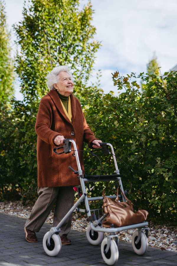 A senior woman with a mobility walker walking on the city streets during autumn day, enjoying the beautiful sunny weather. Elderly lady savoring every moment, living life to fullest.