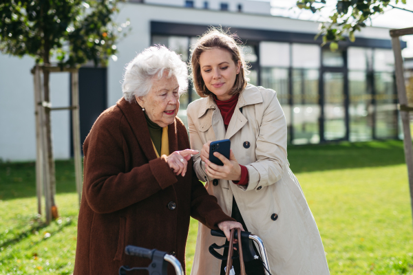 Mature granddaughter teaching grandmother how to use smartphone. Caregiver helping senior lady shopping online on her smartphone.