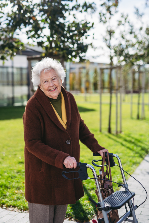 A senior woman with a mobility walker walking on the city streets during autumn day, enjoying the beautiful sunny weather. Elderly lady savoring every moment, living life to fullest.