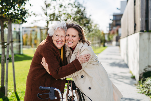 Grandmother and mature granddaughter on a walk in the city park, during a windy autumn day. Caregiver and senior lady enjoying the fall weather, hugging each other.