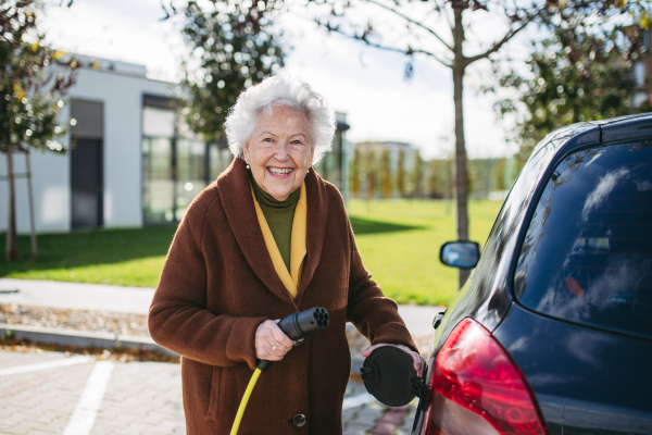 Close up of beautiful senior woman plugging charger in her electric car. Progressive elderly woman charging her electric vehicle on the street.