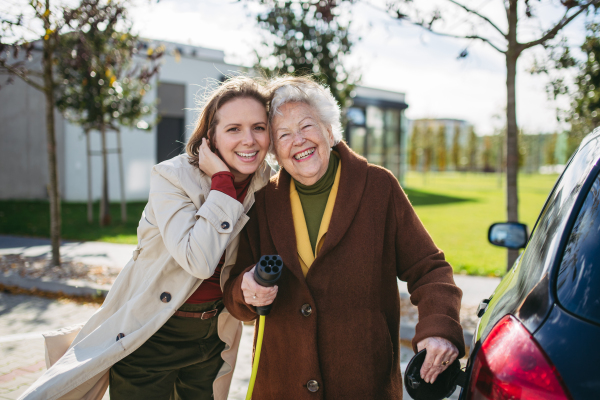 Granddaughter teaching senior woman how to charge new electric car. Progressive grandmother charging her electric vehicle on the street.