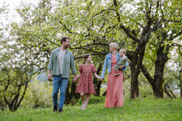 Family portrait with daughter and small toddler or baby, walking outdoors in spring nature. Nuclear family.