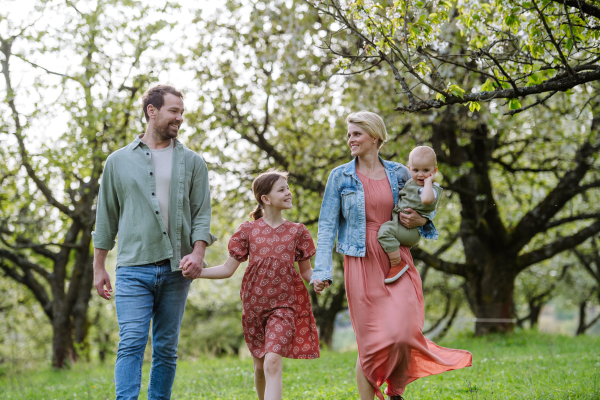 Family portrait with daughter and small toddler or baby, outdoors in spring nature. Nuclear family.