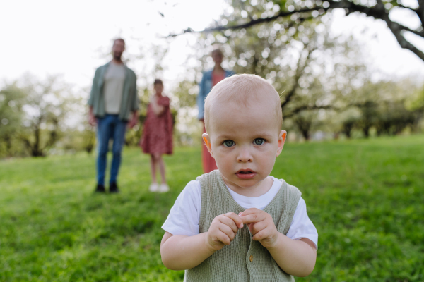 Portrait of cute baby boy standing in front of his family, walking outdoors in spring nature.Nuclear family.