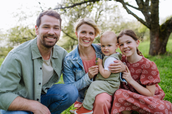 Family portrait with daughter and small toddler or baby, outdoors in spring nature. Nuclear family.