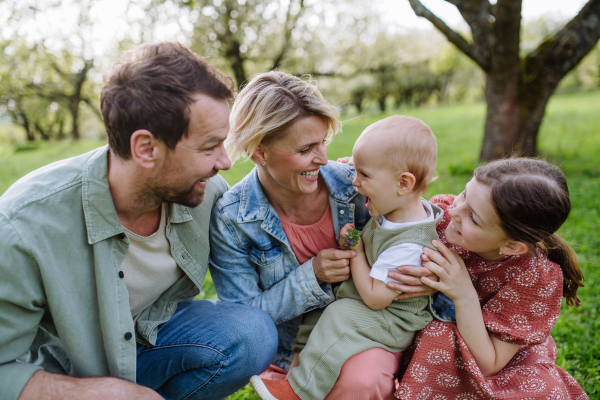 Family portrait with daughter and small toddler or baby, outdoors in spring nature. Nuclear family.