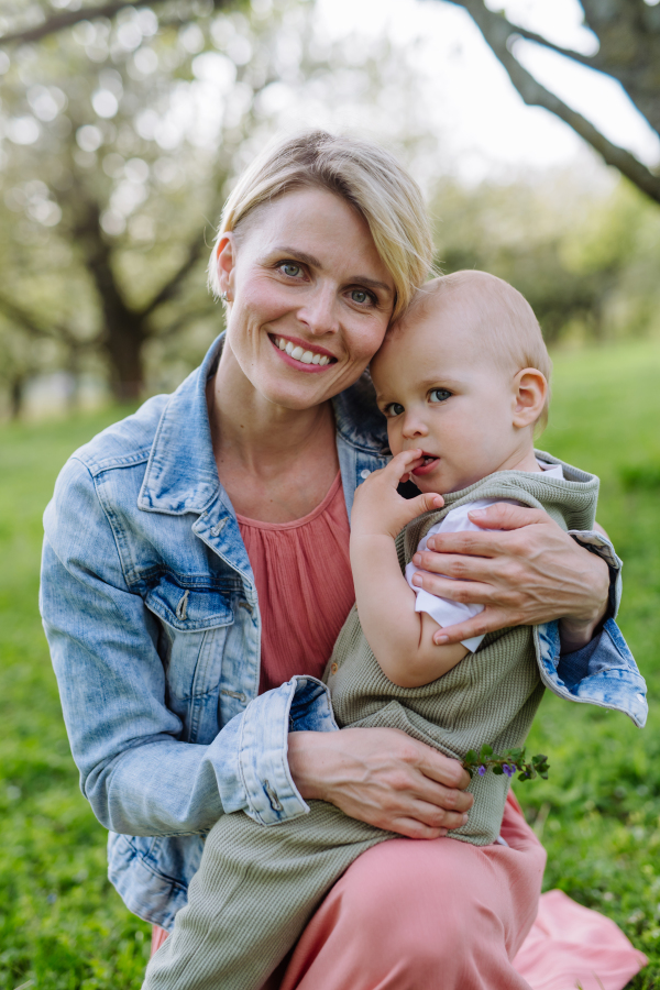 Portrait of beautiful mature first time mother with small toddler, baby, outdoors in spring nature.