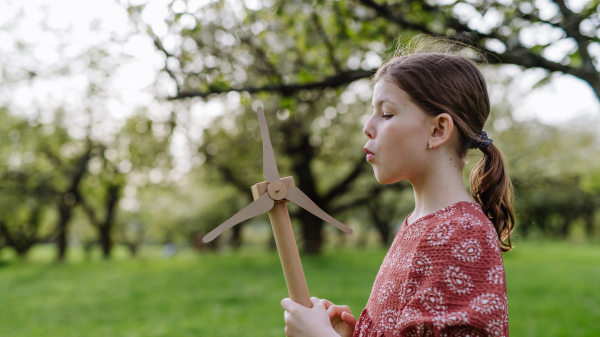 Girl standing outdoors in park, holding wind turbine. Renewable wind energy and sustainable future.