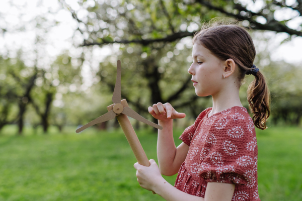 Girl standing outdoors in park, holding wind turbine. Renewable wind energy and sustainable future.