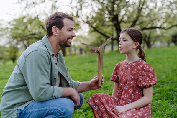 A father teaching daughter about renewable wind energy, sustainable lifestyle. Standing outdoors in park, holding wind turbine.