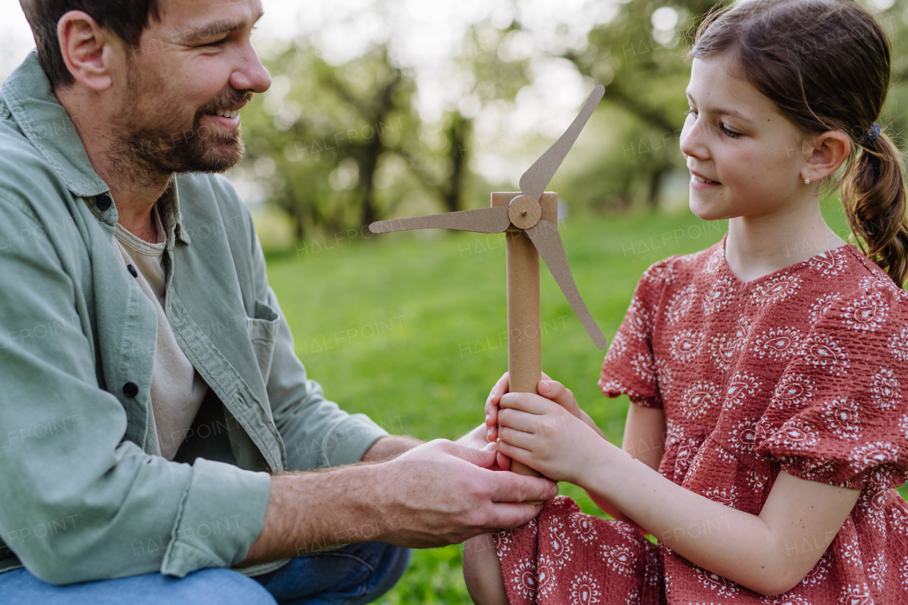 A father teaching daughter about renewable wind energy, sustainable lifestyle. Standing outdoors in park, holding wind turbine.