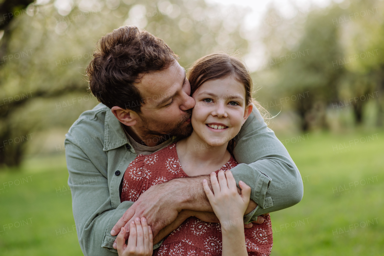 A father hugging his daughter in spring in nature, kissing her on cheek. Father's day concept.