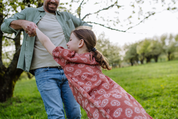 Father spinning daughter around, holding her under armpits. Dad and girl having fun and laughing outdoor. Father's day concept.