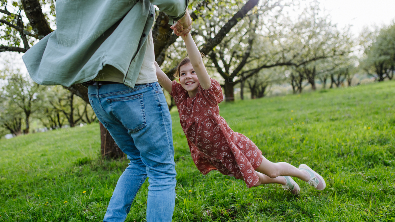 Father spinning daughter around, holding her under armpits. Dad and girl having fun and laughing outdoor. Father's day concept.