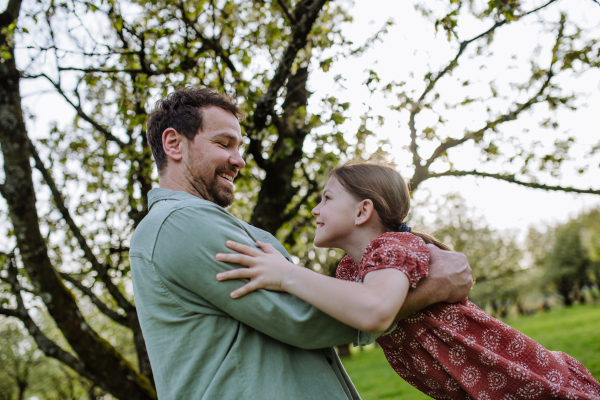 Father spinning daughter around, holding her under armpits. Dad and girl having fun and laughing outdoor. Father's day concept.