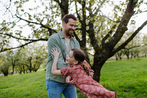 Father spinning daughter around, holding her under armpits. Dad and girl having fun and laughing outdoor. Father's day concept.