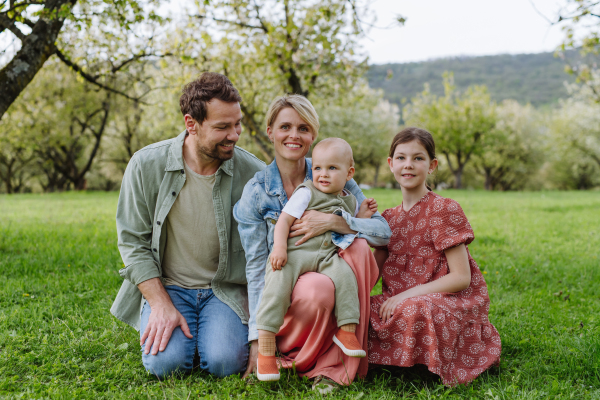 Family portrait with daughter and small toddler or baby, outdoors in spring nature. Nuclear family.