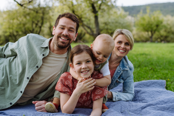 Family portrait with daughter and small toddler, baby, lying on picnic blanket outdoors in spring nature.