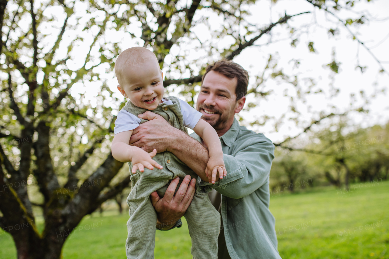 A father holding little baby, playing, having fun during warm spring day. Father's day concept.