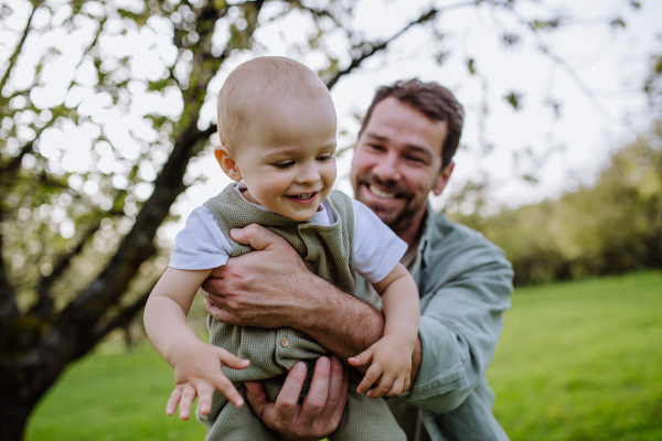 A father holding little baby, playing, having fun during warm spring day. Father's day concept.