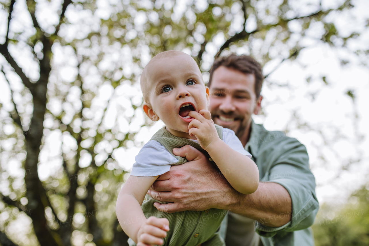 A father holding little baby, playing, having fun during warm spring day. Father's day concept.