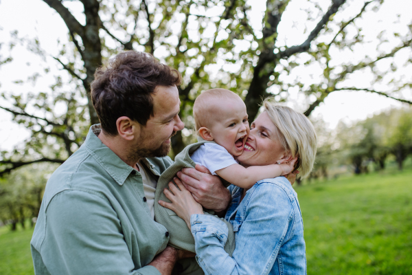 New parents holding small toddler, baby, outdoors in spring nature. An older first-time parents.