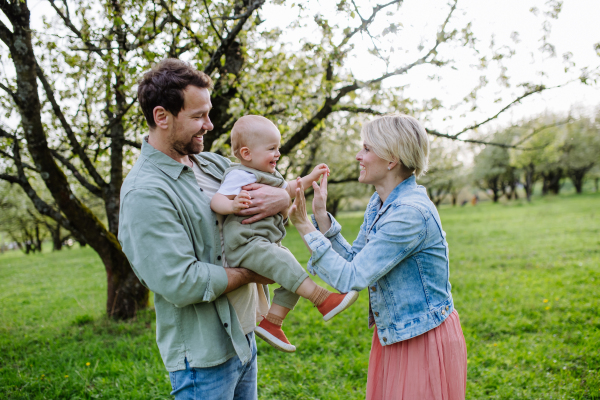 New parents holding small toddler, baby, outdoors in spring nature. An older first-time parents.