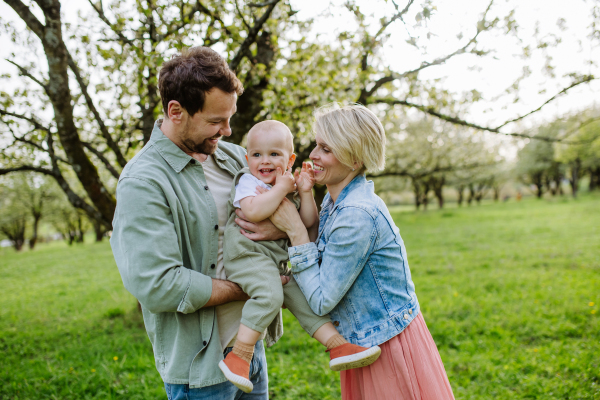 New parents holding small toddler, baby, outdoors in spring nature. An older first-time parents.