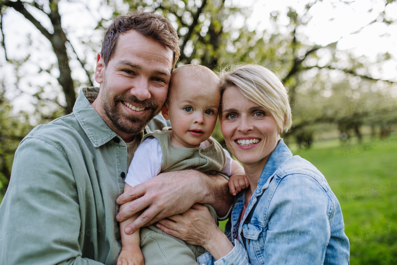 New parents holding small toddler, baby, outdoors in spring nature. An older first-time parents.