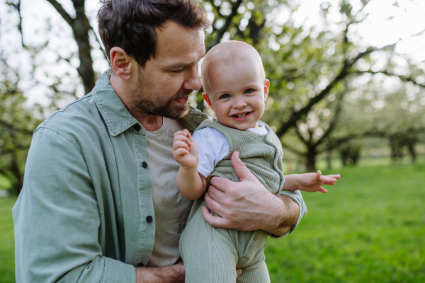 A father holding little baby, playing, having fun during warm spring day. Father's day concept.