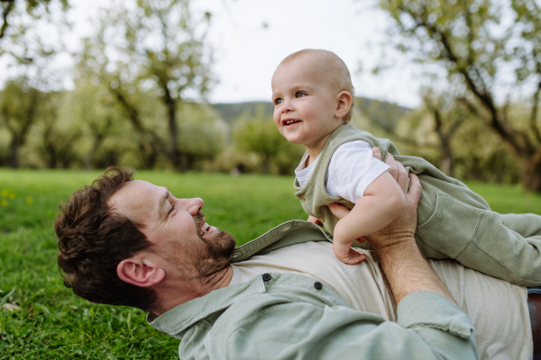 A father lying and playing with little baby, having fun in grass during warm spring day. Father's day concept.