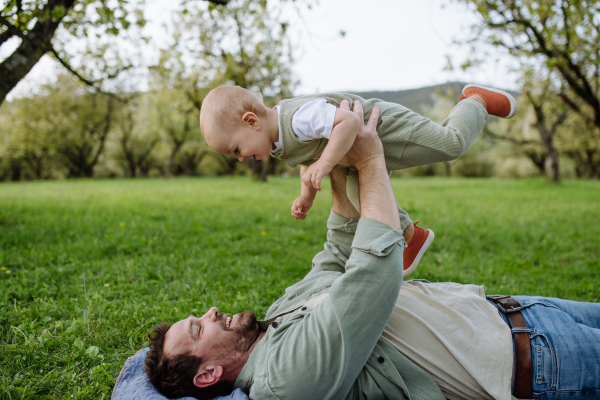 A father holding little baby, playing, having fun during warm spring day. Father's day concept.