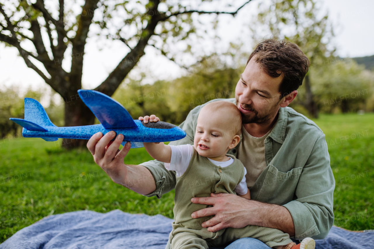 Father and toddler playing with foam glider plane. A Single dad having fun with baby during warm spring day. Father's day concept.