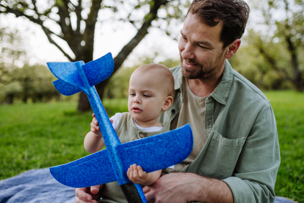 Father and toddler playing with foam glider plane. A Single dad having fun with baby during warm spring day. Father's day concept.