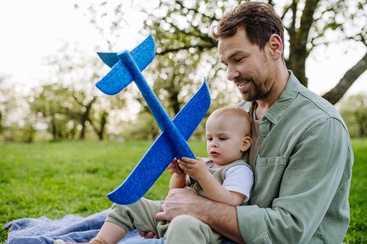 Father and toddler playing with foam glider plane. A Single dad having fun with baby during warm spring day. Father's day concept.