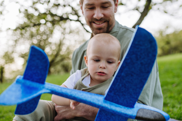 Father and toddler playing with foam glider plane. A Single dad having fun with baby during warm spring day. Father's day concept.