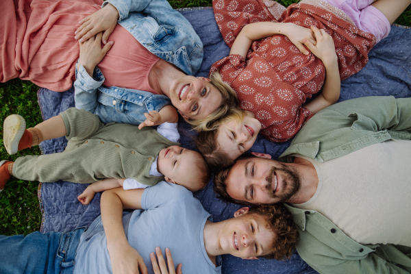 Top view of family lying on picnic blanket portrait with two parents, son, daughter and small toddler outdoors in spring nature.