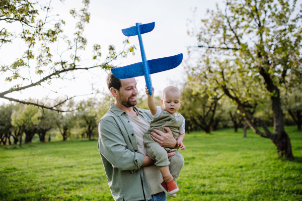 Father and toddler playing with foam glider plane. A Single dad having fun with baby during warm spring day. Father's day concept.