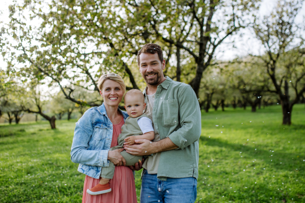 New parents holding small toddler, baby, outdoors in spring nature. An older first-time parents.