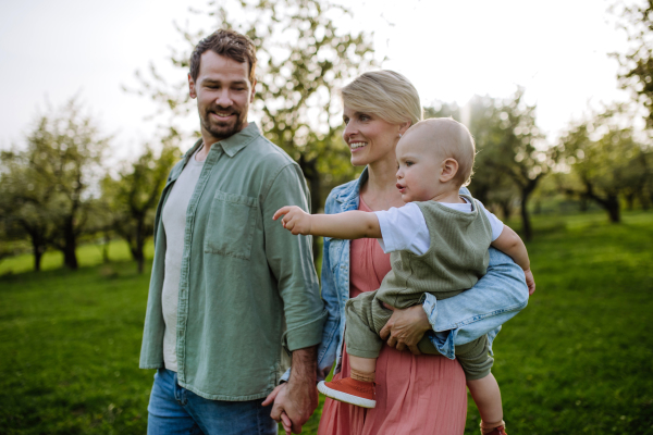 New parents holding small toddler, baby, outdoors in spring nature. An older first-time parents.