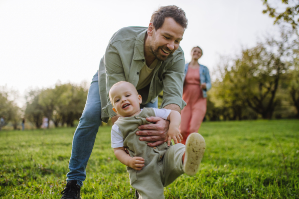 First steps for little toddler. A father supporting baby while walking in soft spring grass on meadow. Father's day concept.