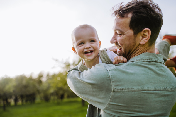 A father holding little baby, playing, having fun during warm spring day. Father's day concept.