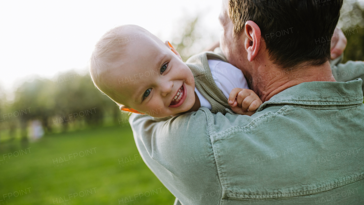 A father holding little baby, playing, having fun during warm spring day. Father's day concept.