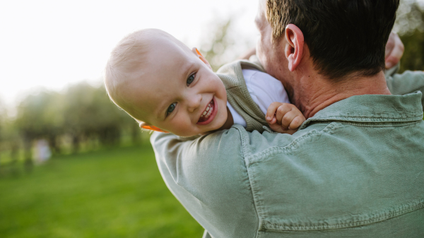 A father holding little baby, playing, having fun during warm spring day. Father's day concept.