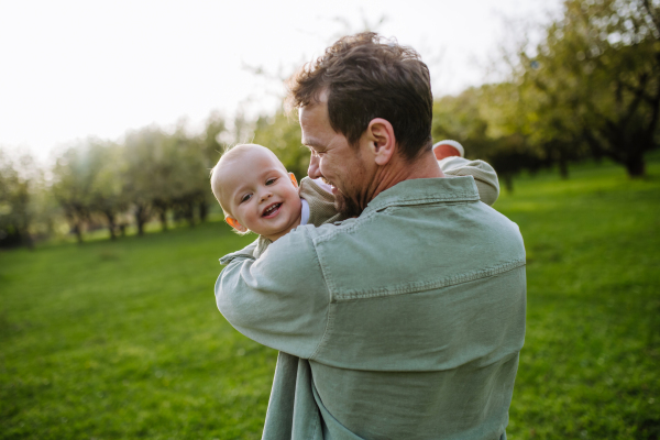 A father holding little baby, playing, having fun during warm spring day. Father's day concept.