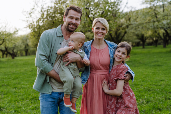 Family portrait with daughter and small toddler or baby, outdoors in spring nature. Nuclear family.