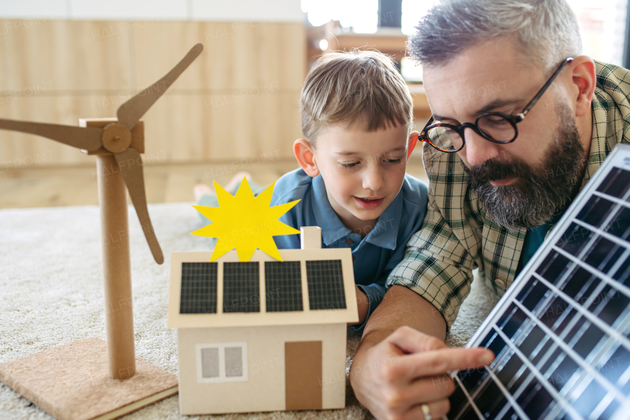 Father explaining renewable energy, solar power and teaching about sustainable lifestyle his young son. Playing with model of house with solar panels. Learning through play.