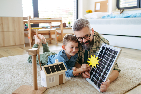 Father explaining renewable energy, solar power and teaching about sustainable lifestyle his young son. Playing with model of house with solar panels. Learning through play.