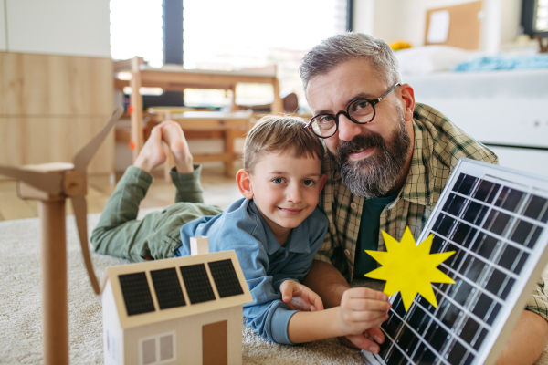 Father explaining renewable energy, solar power and teaching about sustainable lifestyle his young son. Playing with model of house with solar panels. Learning through play.